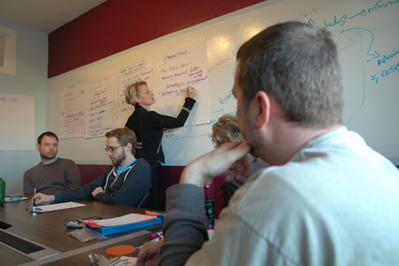 photo of woman writing on a white board while everyone watches