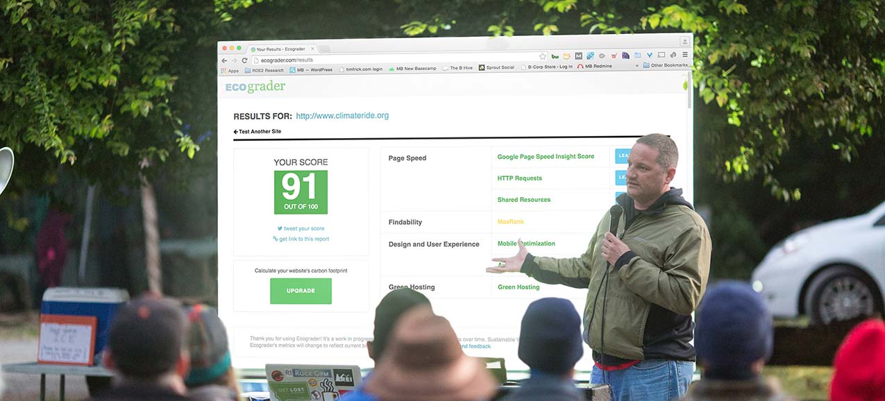 Photo of speaker holding microphone in front of a screen showing an Ecograder report.